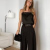 Femme portant un top en satin noir avec dentelle et un pantalon large noir à strass, accompagné d’une pochette brillante.
