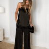 Femme portant un top en satin noir avec dentelle et un pantalon large noir à strass, accompagné d’une pochette brillante.