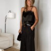 Femme portant un top en satin noir avec dentelle et un pantalon large noir à strass, accompagné d’une pochette brillante.