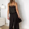 Femme portant un top en satin noir avec dentelle et un pantalon large noir à strass, accompagné d’une pochette brillante.
