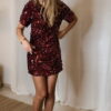 Femme portant une robe courte à sequins bordeaux, coupe ajustée et manches courtes, assortie de chaussures à talons noirs.