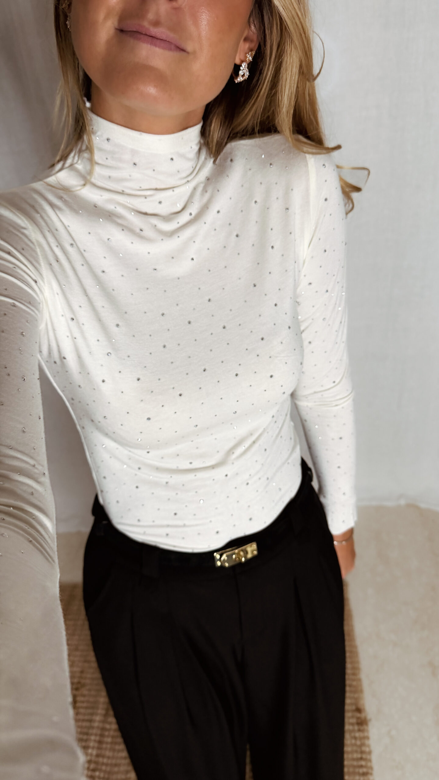 « Femme portant un top écru à col roulé orné de strass, associé à un pantalon noir élégant »