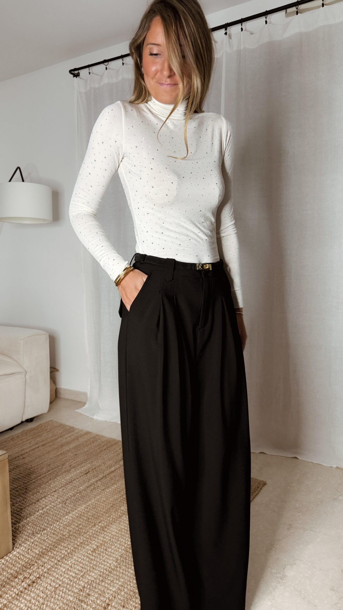 « Femme portant un top écru à col roulé orné de strass, associé à un pantalon noir élégant »