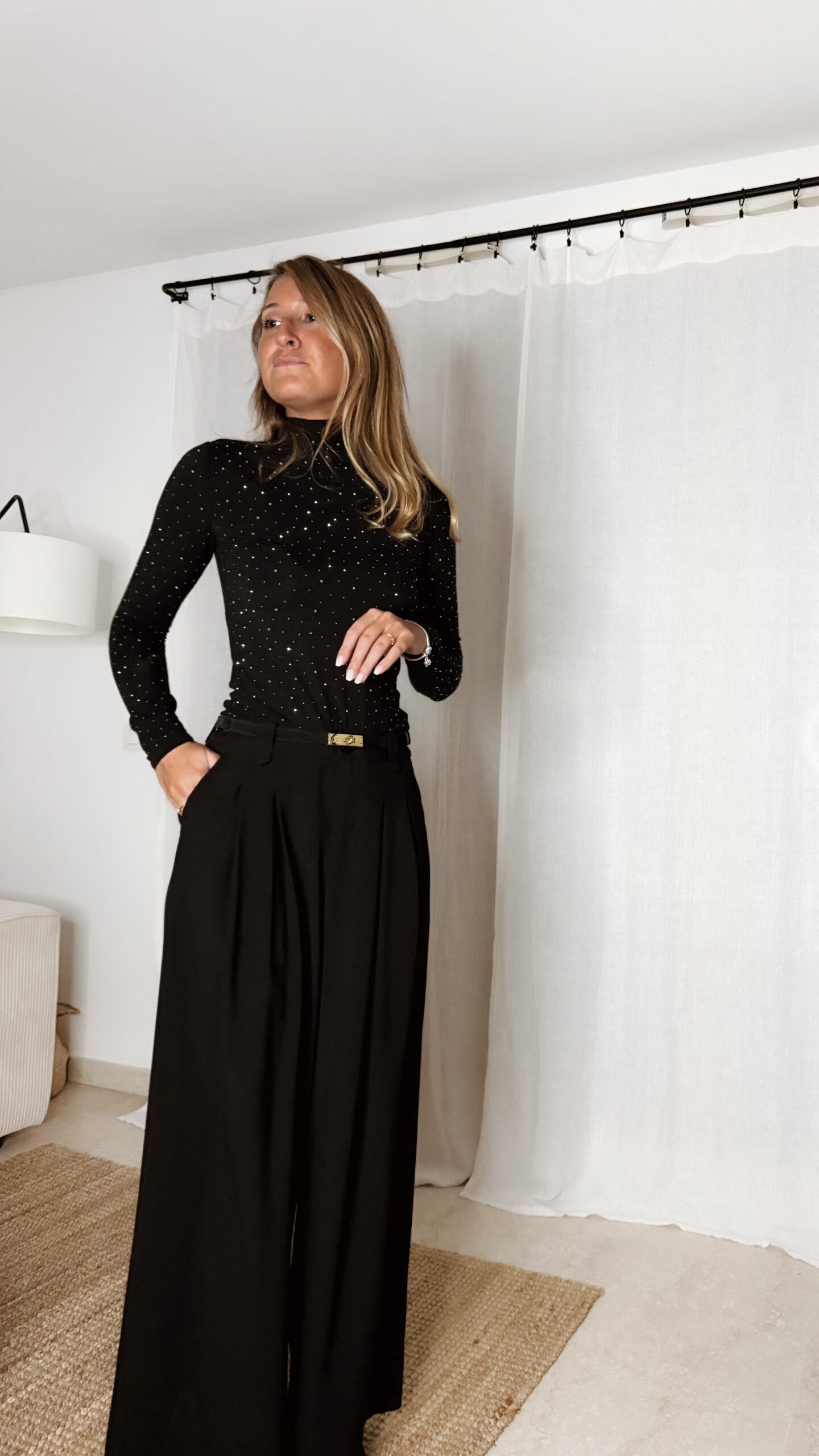 « Femme portant un top noir à col roulé orné de strass, associé à un pantalon noir large et une pochette à sequins »