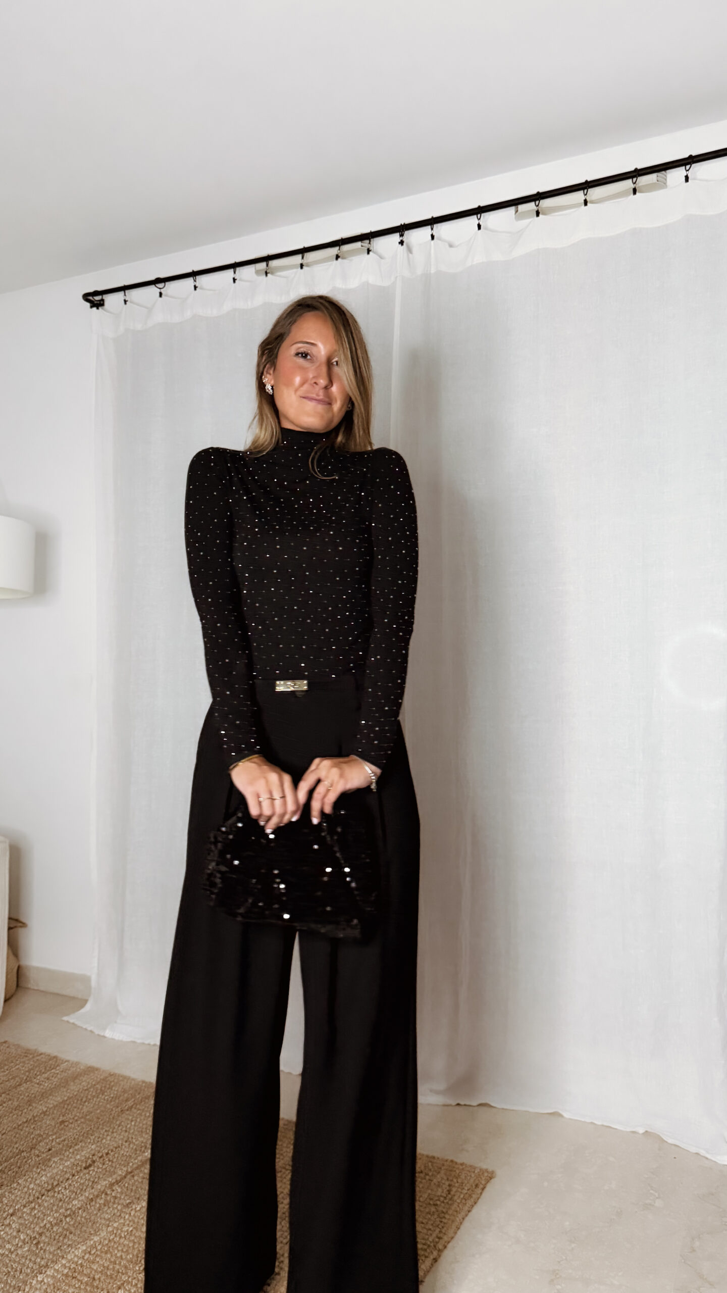 « Femme portant un top noir à col roulé orné de strass, associé à un pantalon noir large et une pochette à sequins »
