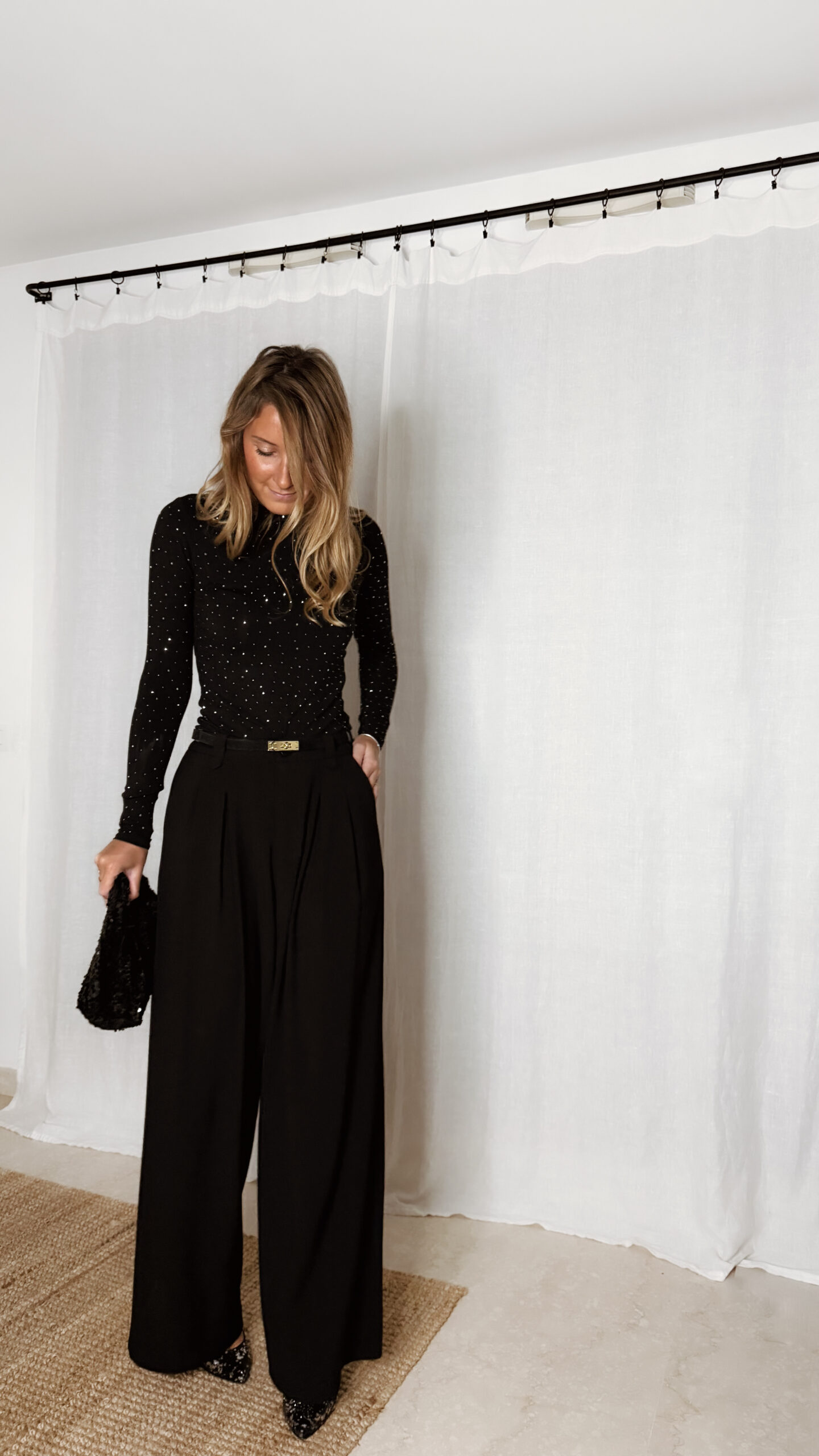 « Femme portant un top noir à col roulé orné de strass, associé à un pantalon noir large et une pochette à sequins »