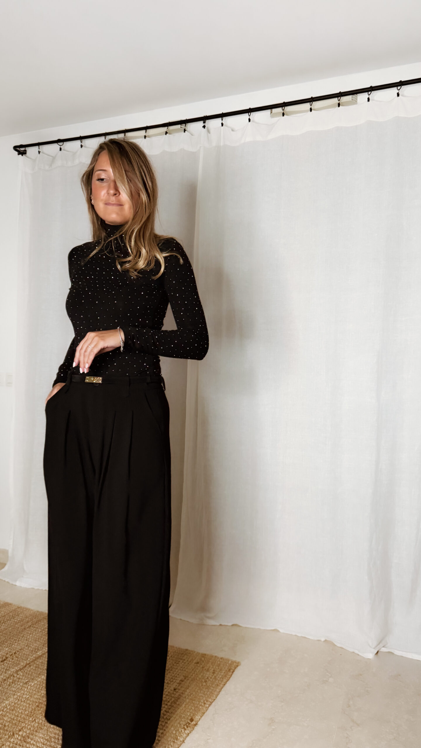 « Femme portant un top noir à col roulé orné de strass, associé à un pantalon noir large et une pochette à sequins »