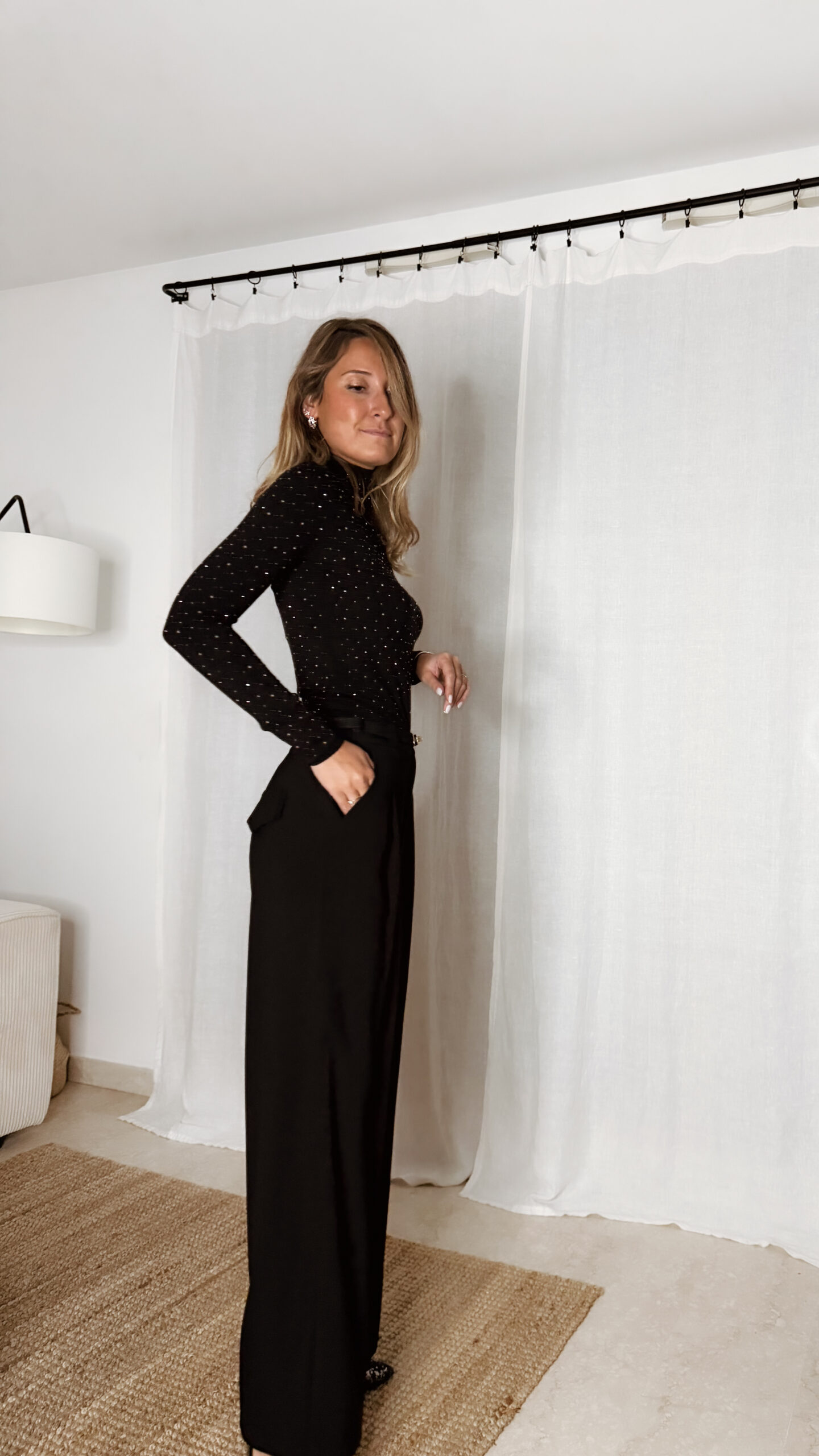 « Femme portant un top noir à col roulé orné de strass, associé à un pantalon noir large et une pochette à sequins »