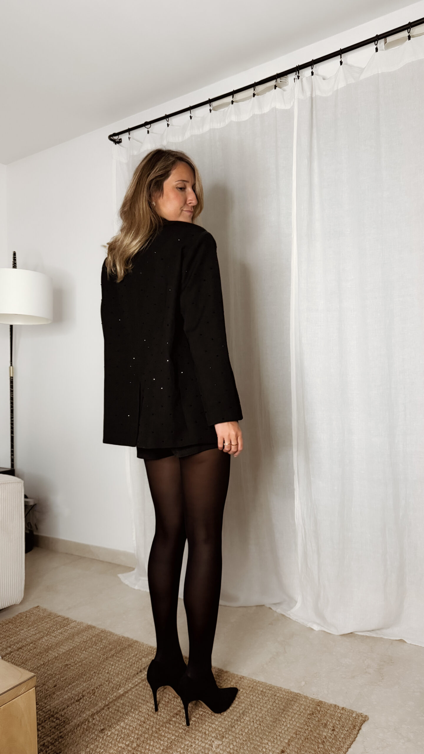 Femme portant un blazer noir à strass avec collants noirs et escarpins, tenue élégante et chic de soirée.