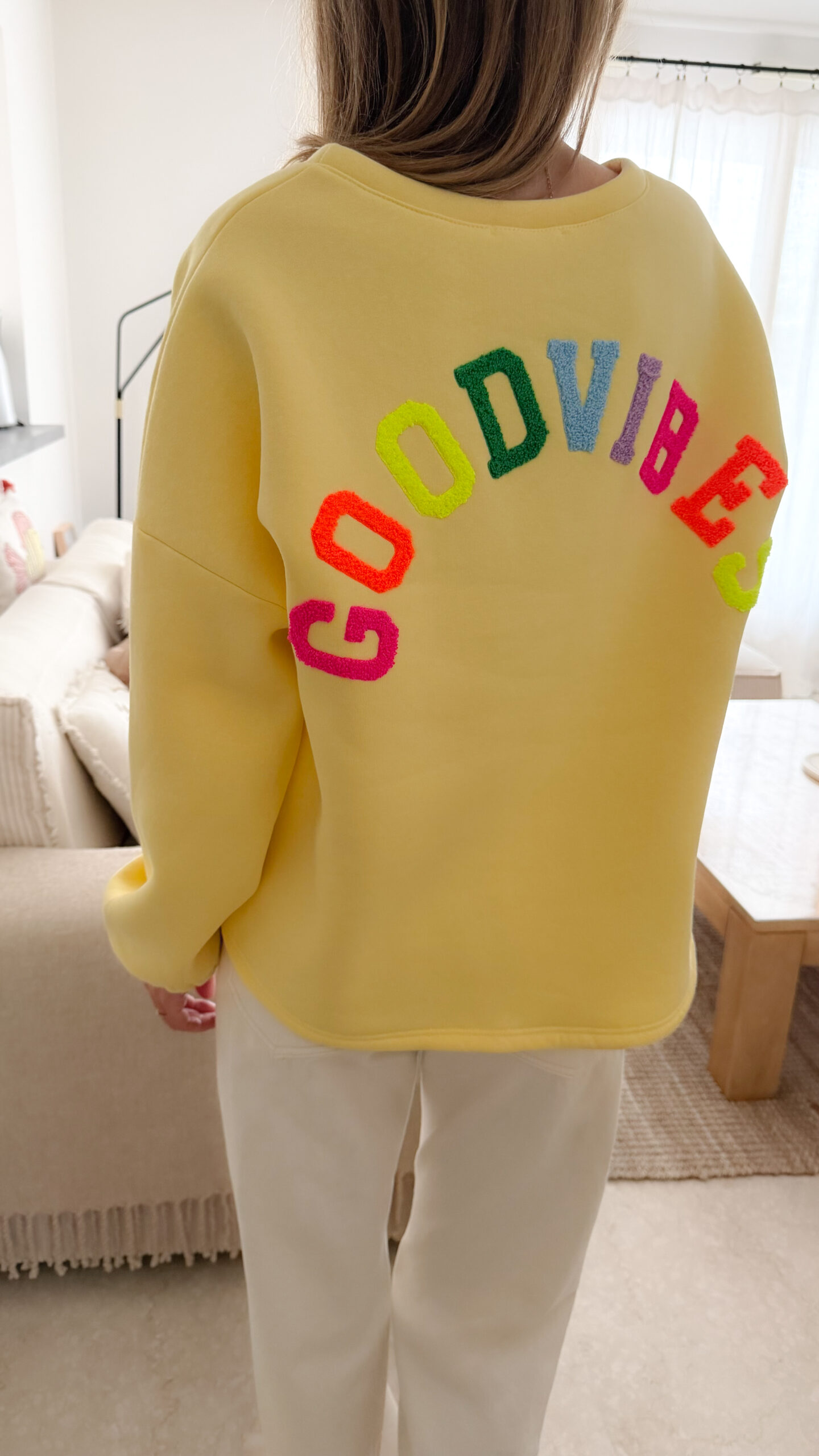 Sweat jaune à coupe ample, vu de dos, avec l’inscription brodée multicolore « GOOD VIBES ».