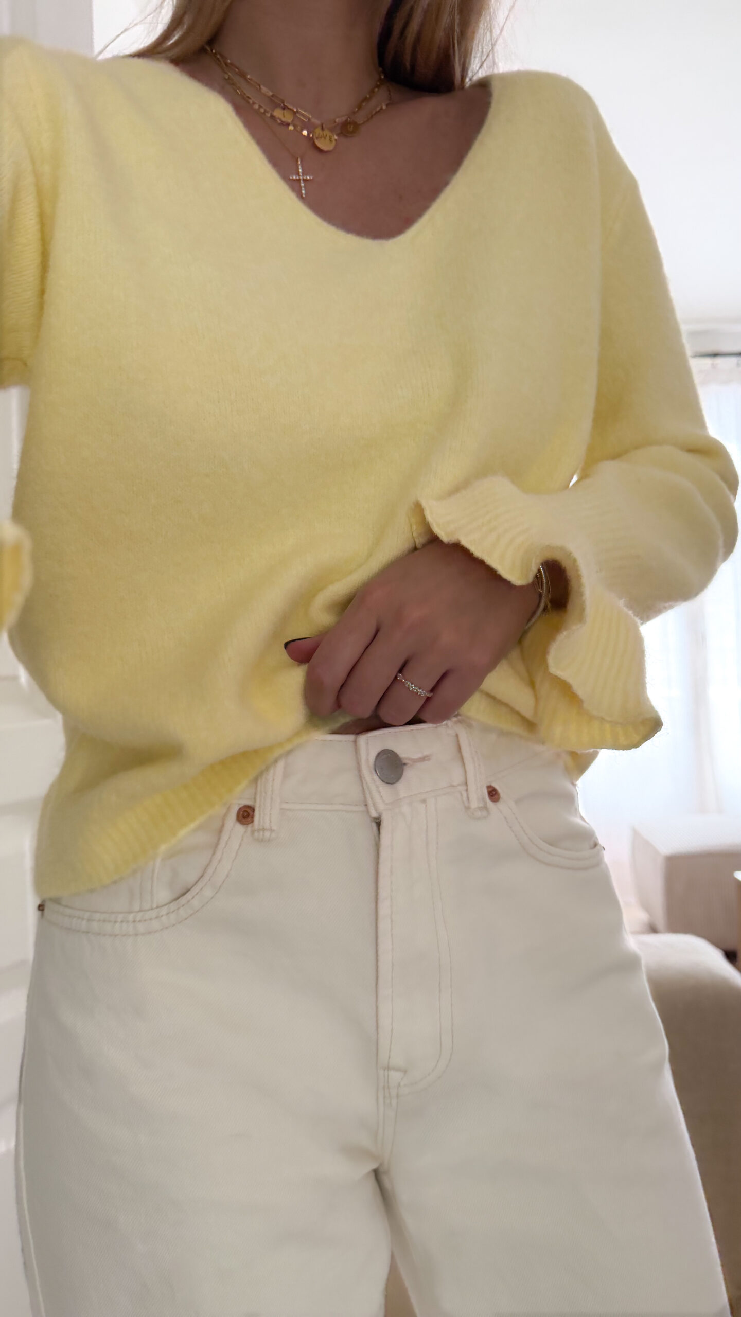 Pull jaune à col V, coupe droite, porté avec un pantalon clair, manches longues avec poignets volantés.