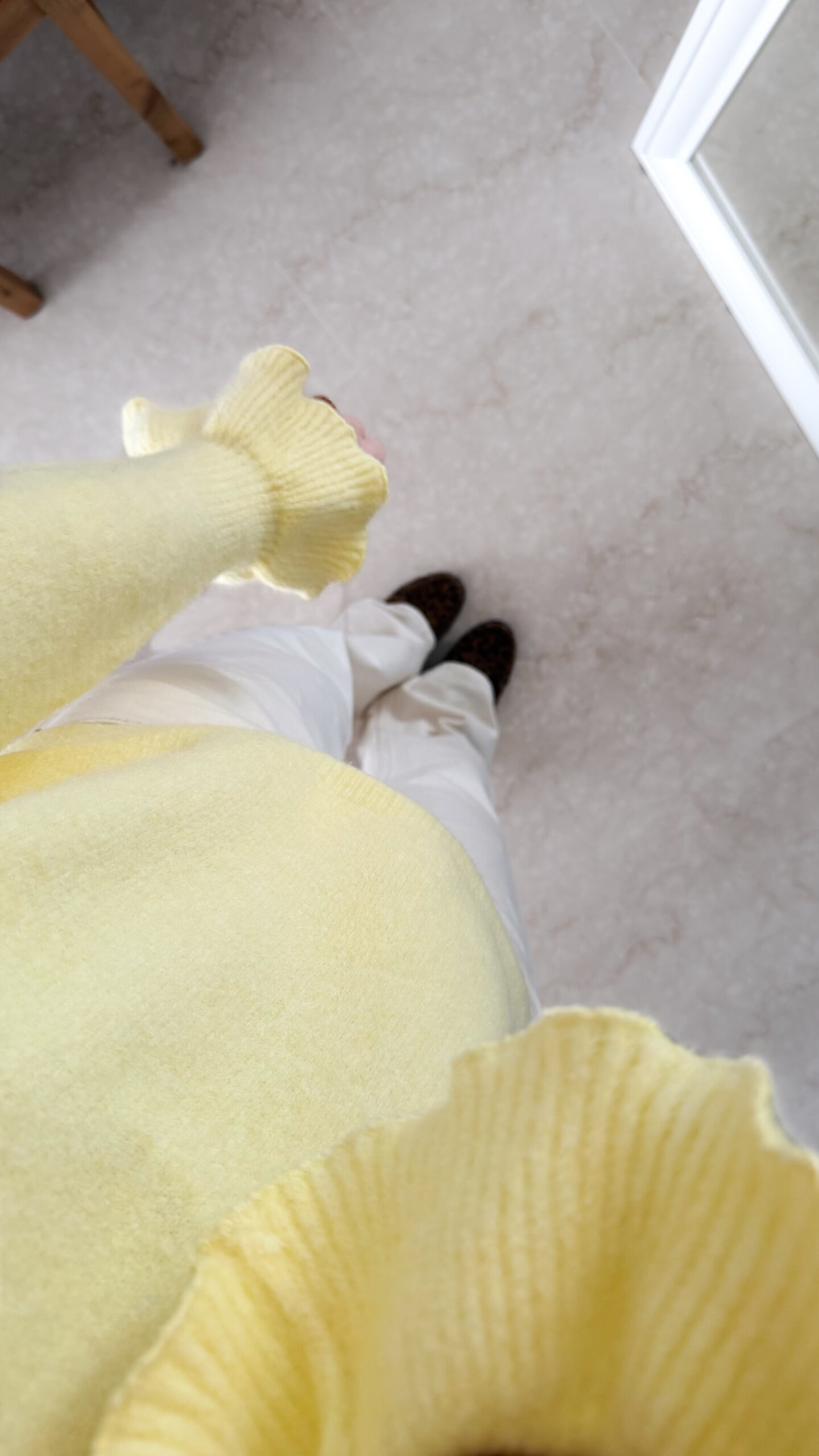 Pull jaune à col V, coupe droite, porté avec un pantalon clair, manches longues avec poignets volantés.
