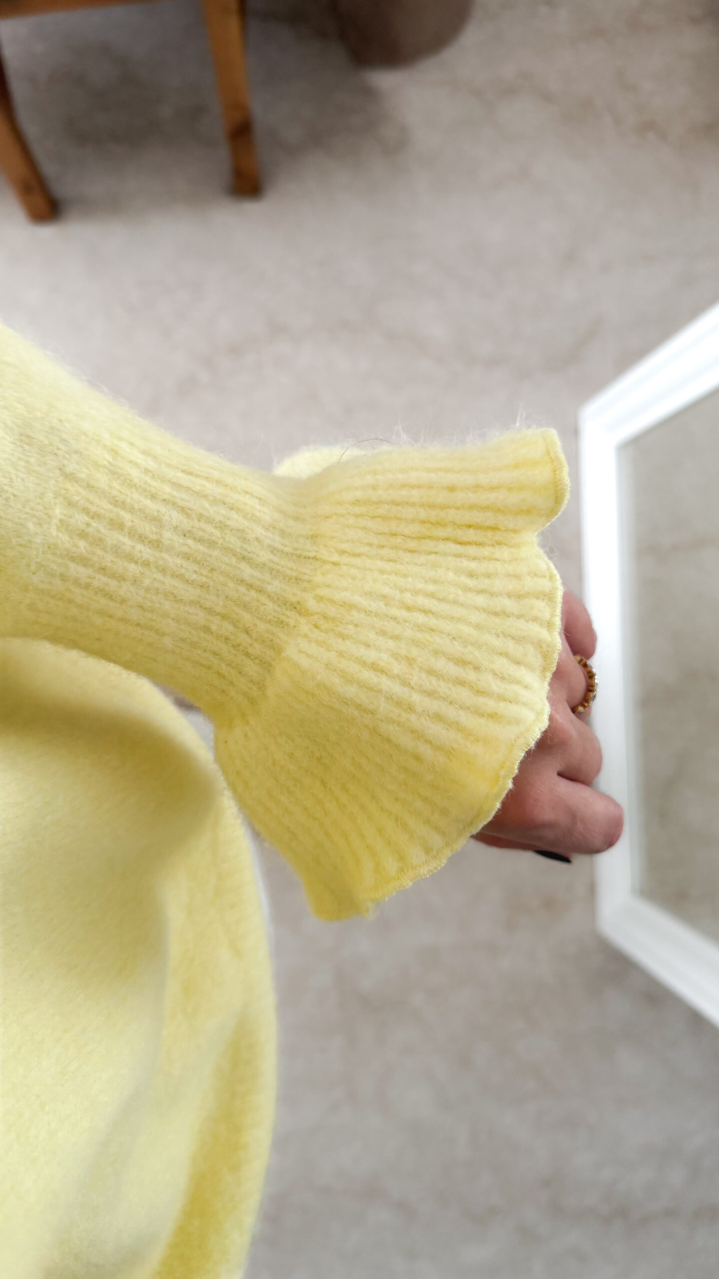 Pull jaune à col V, coupe droite, porté avec un pantalon clair, manches longues avec poignets volantés.