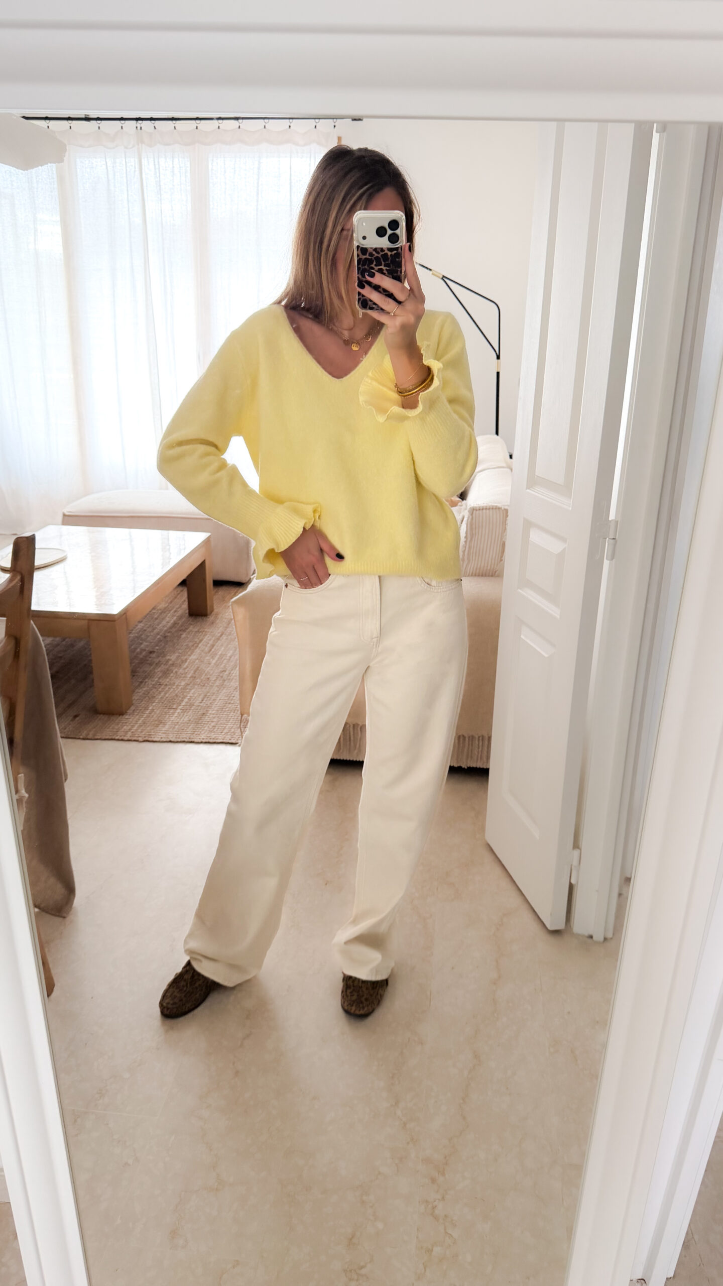 Pull jaune à col V, coupe droite, porté avec un pantalon clair, manches longues avec poignets volantés.