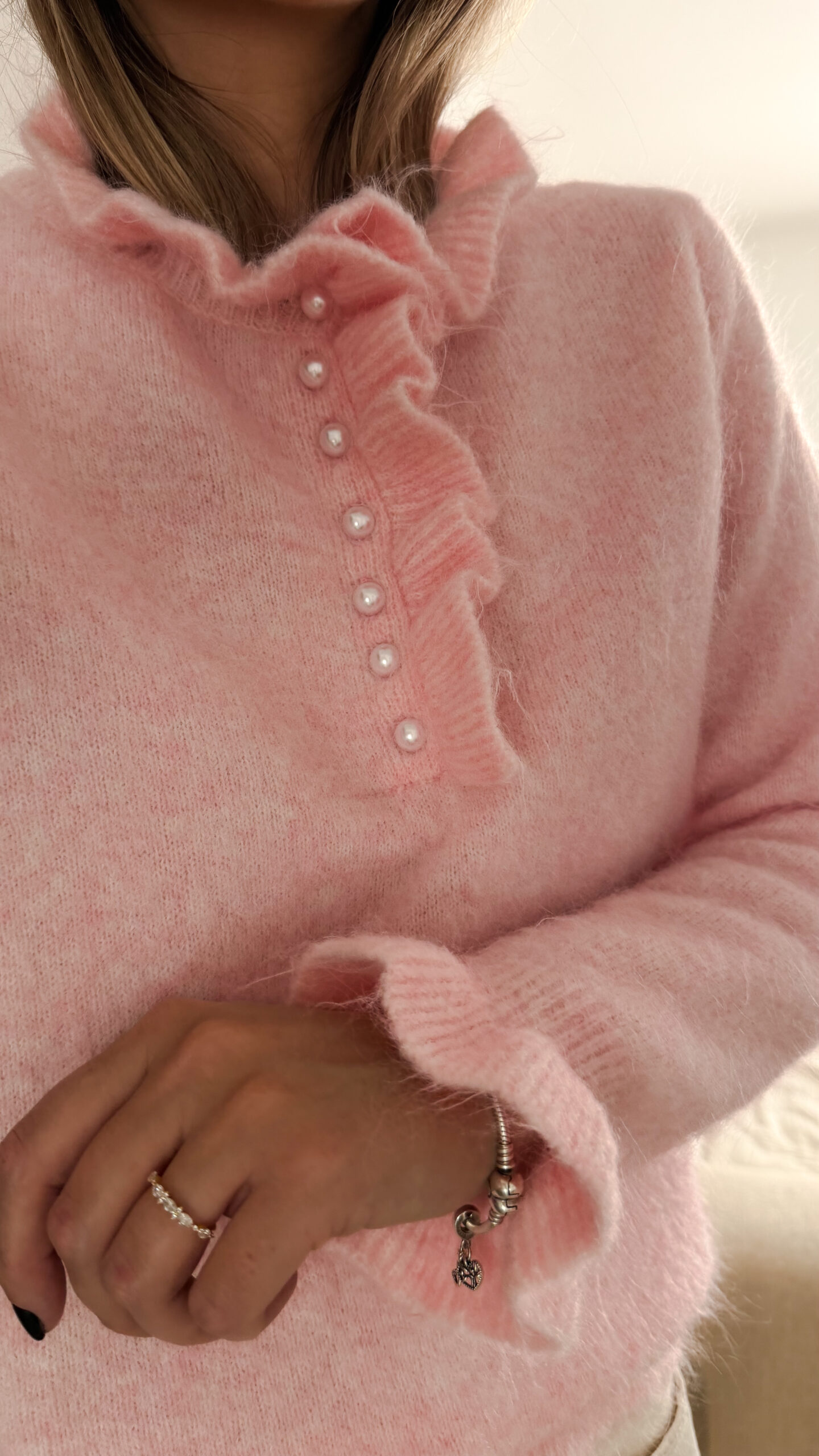 Pull rose en maille douce avec col volanté et boutons perles, porté avec un pantalon clair