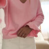 Pull rose à col V, coupe droite, porté avec un pantalon clair, détails volants aux poignets.