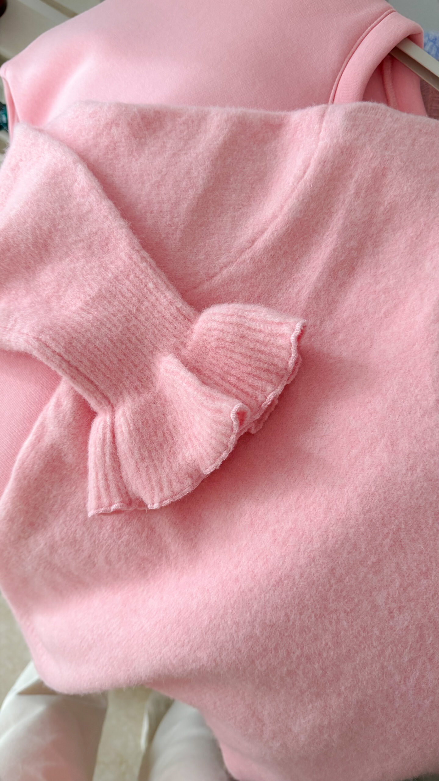 Pull rose à col V, coupe droite, porté avec un pantalon clair, détails volants aux poignets.