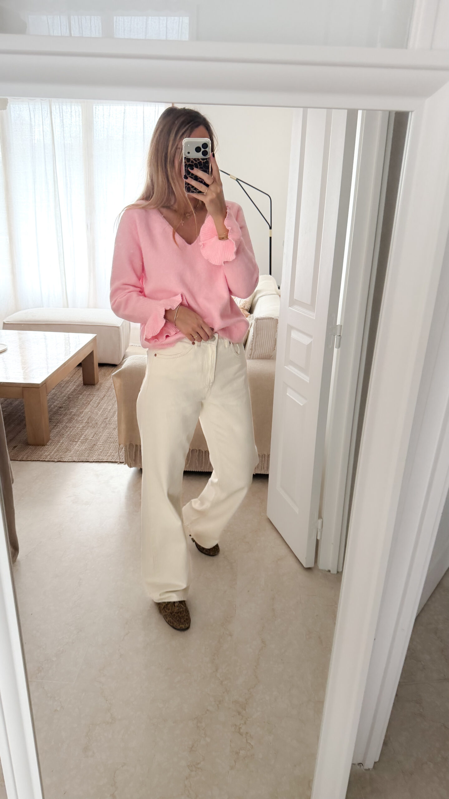 Pull rose à col V, coupe droite, porté avec un pantalon clair, détails volants aux poignets.