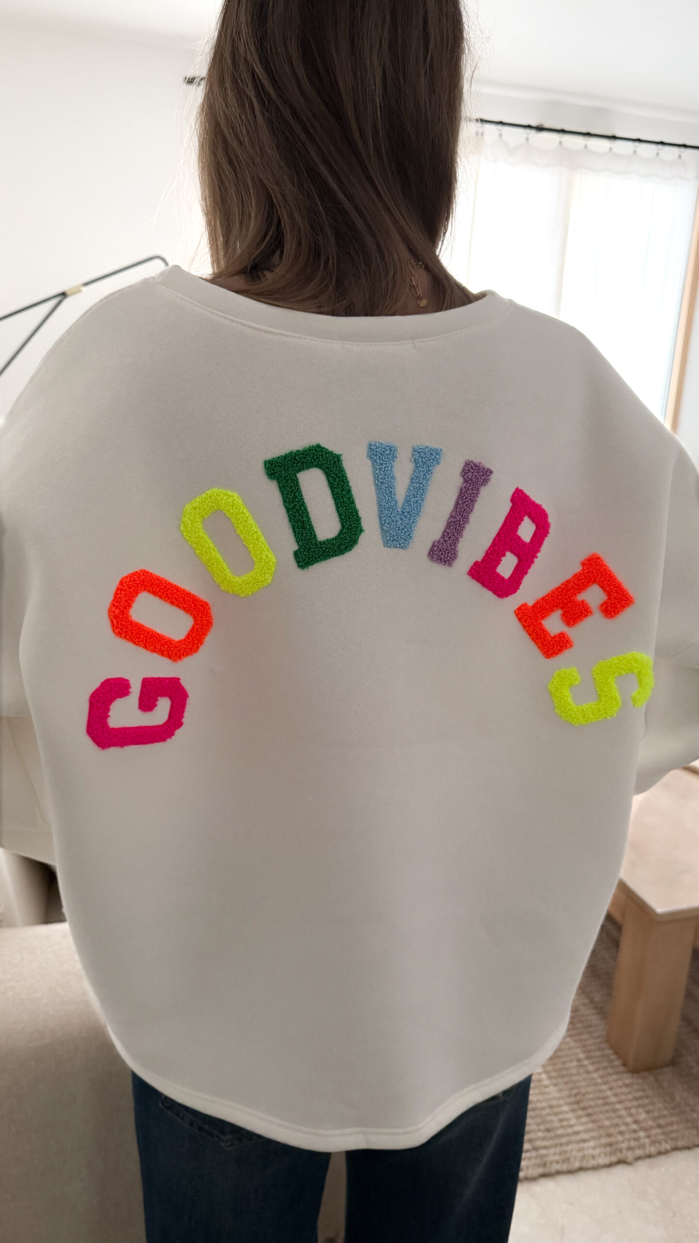 Sweat blanc à coupe ample, vu de dos, avec l’inscription brodée multicolore « GOOD VIBES ».