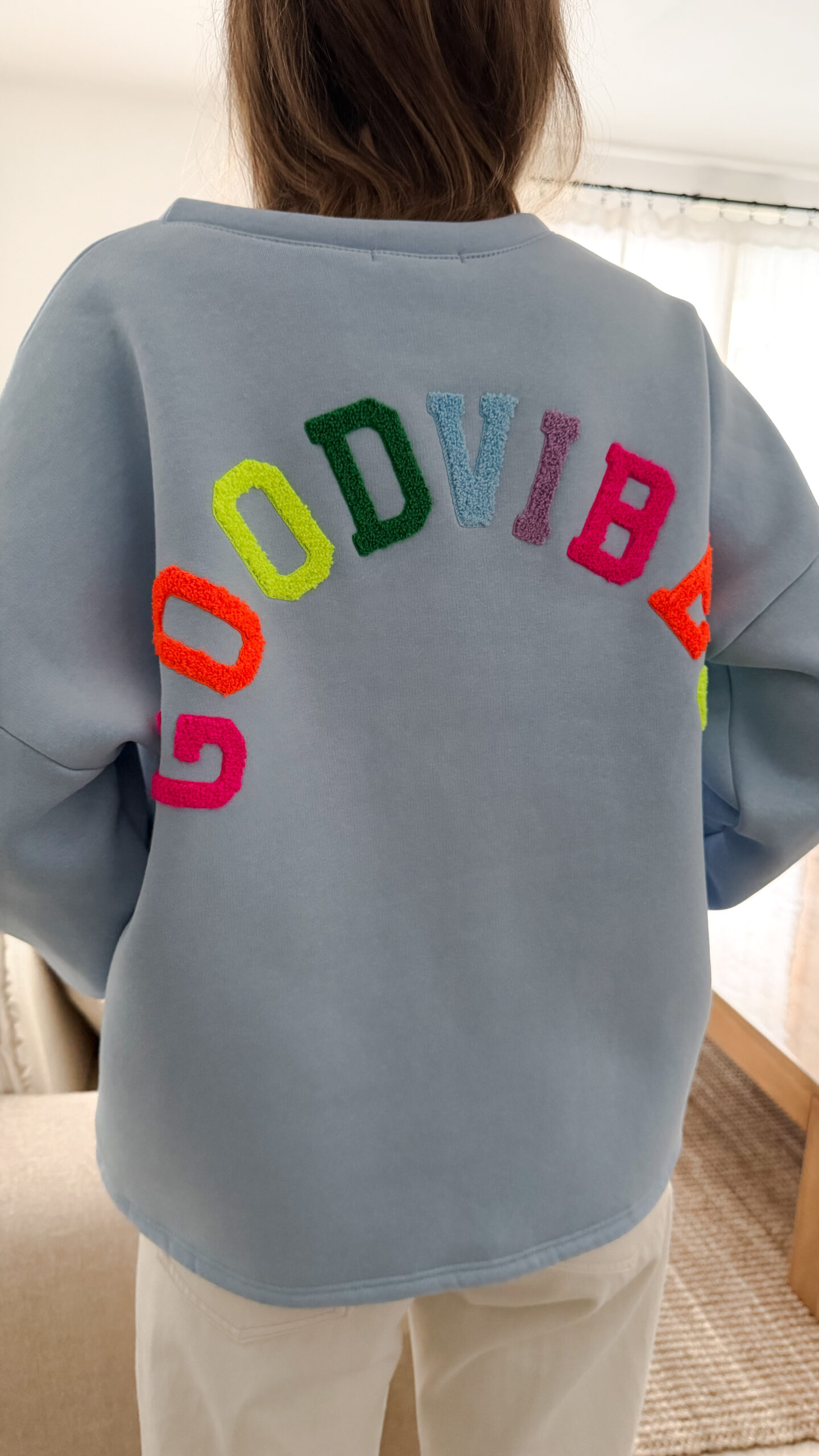 Sweat bleu ciel à coupe ample, vu de dos, avec l’inscription brodée multicolore « GOOD VIBES ».