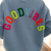 Sweat bleu à coupe ample, vu de dos, avec l’inscription brodée multicolore « GOOD VIBES ».