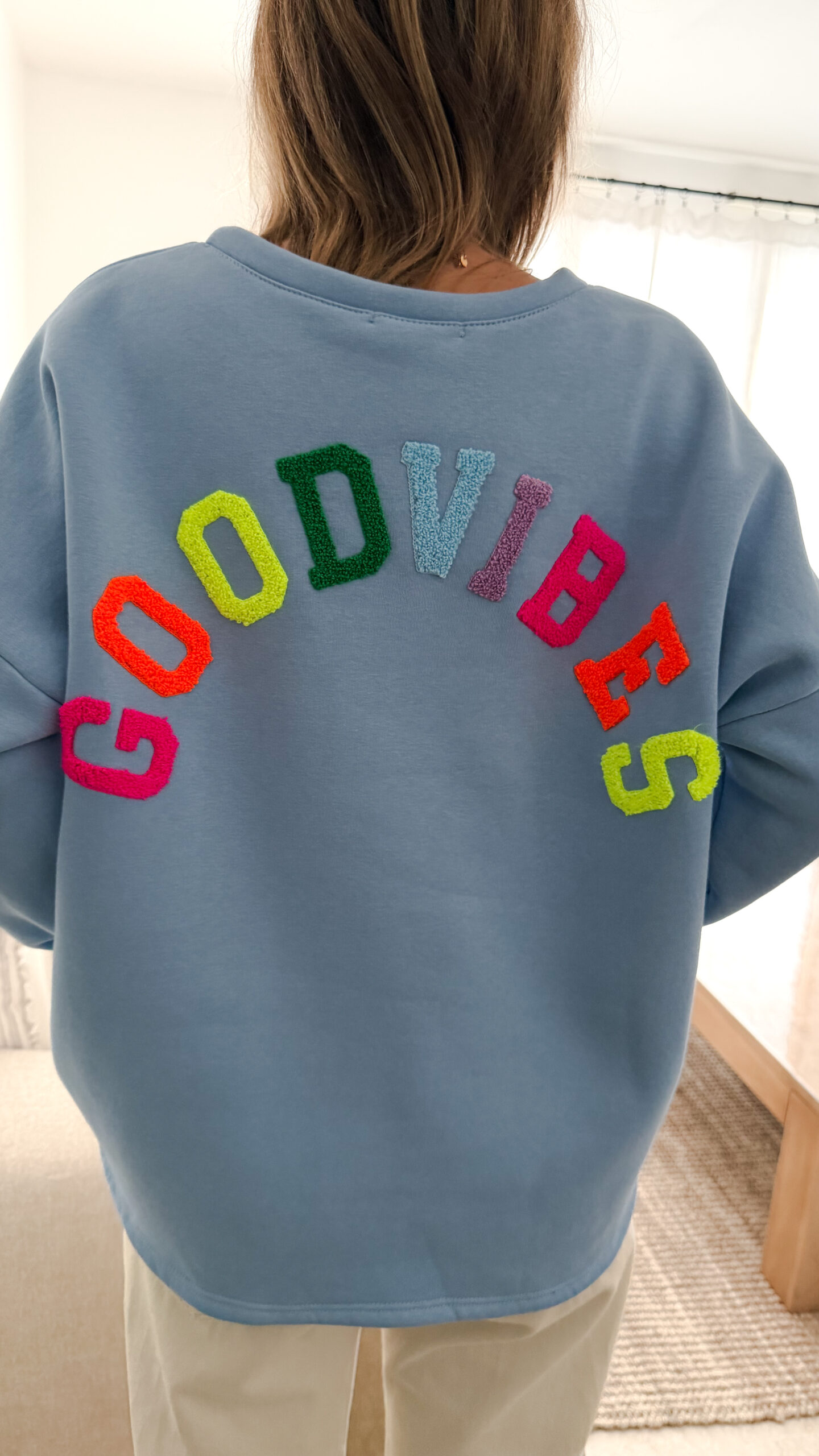 Sweat bleu à coupe ample, vu de dos, avec l’inscription brodée multicolore « GOOD VIBES ».