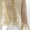 Blouse femme jaune pastel en tissu léger avec volants, manches évasées et col à nouer, portée avec un short blanc.