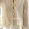 Blouse femme jaune pastel en tissu léger avec volants, manches évasées et col à nouer, portée avec un short blanc.