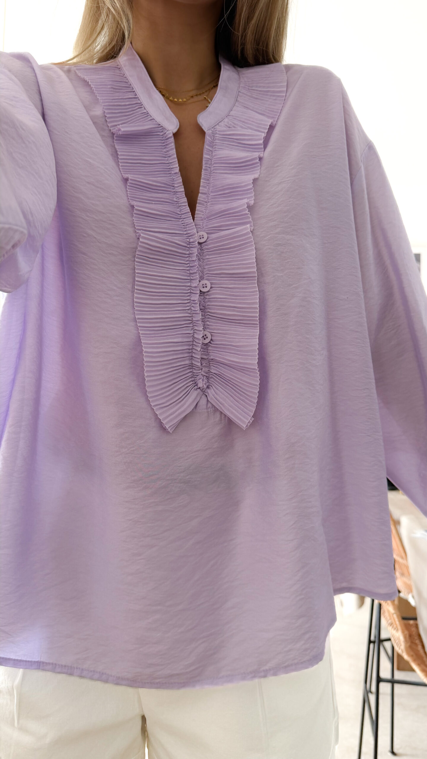 Blouse femme lilas pastel avec plastron plissé, boutons et manches longues, portée avec un bas clair.