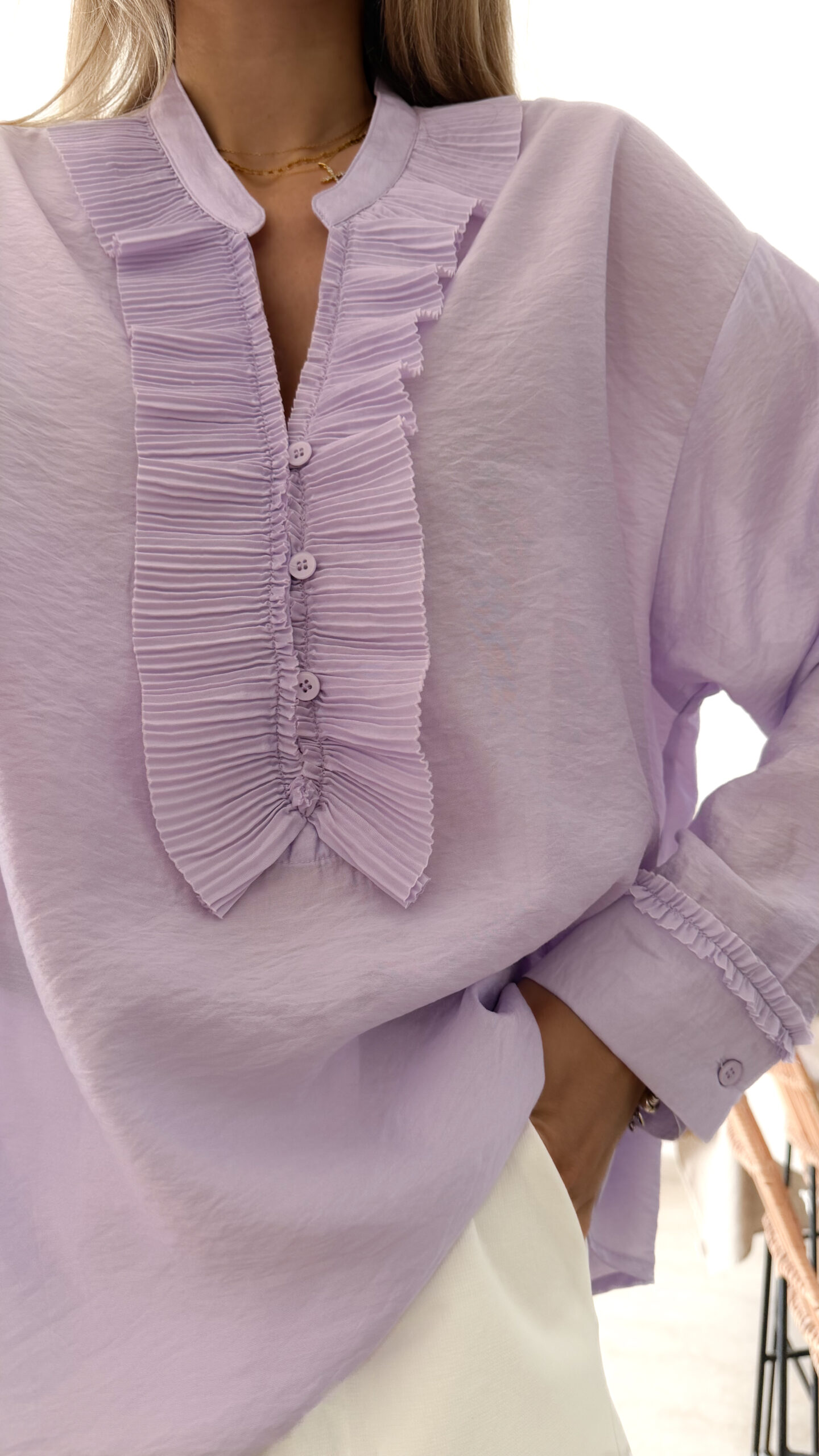 Blouse femme lilas pastel avec plastron plissé, boutons et manches longues, portée avec un bas clair.