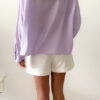 Blouse femme lilas pastel avec plastron plissé, boutons et manches longues, portée avec un bas clair.