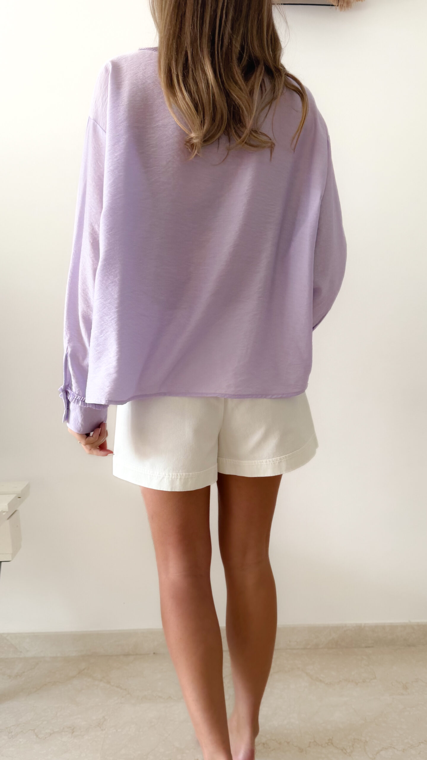 Blouse femme lilas pastel avec plastron plissé, boutons et manches longues, portée avec un bas clair.