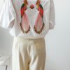 Chemise blanche femme avec broderie de deux perroquets colorés dans le dos, portée avec un pantalon jaune pâle
