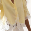 Chemise femme jaune pastel avec dentelle blanche en bas et sur les manches, manches courtes, portée avec un short blanc.
