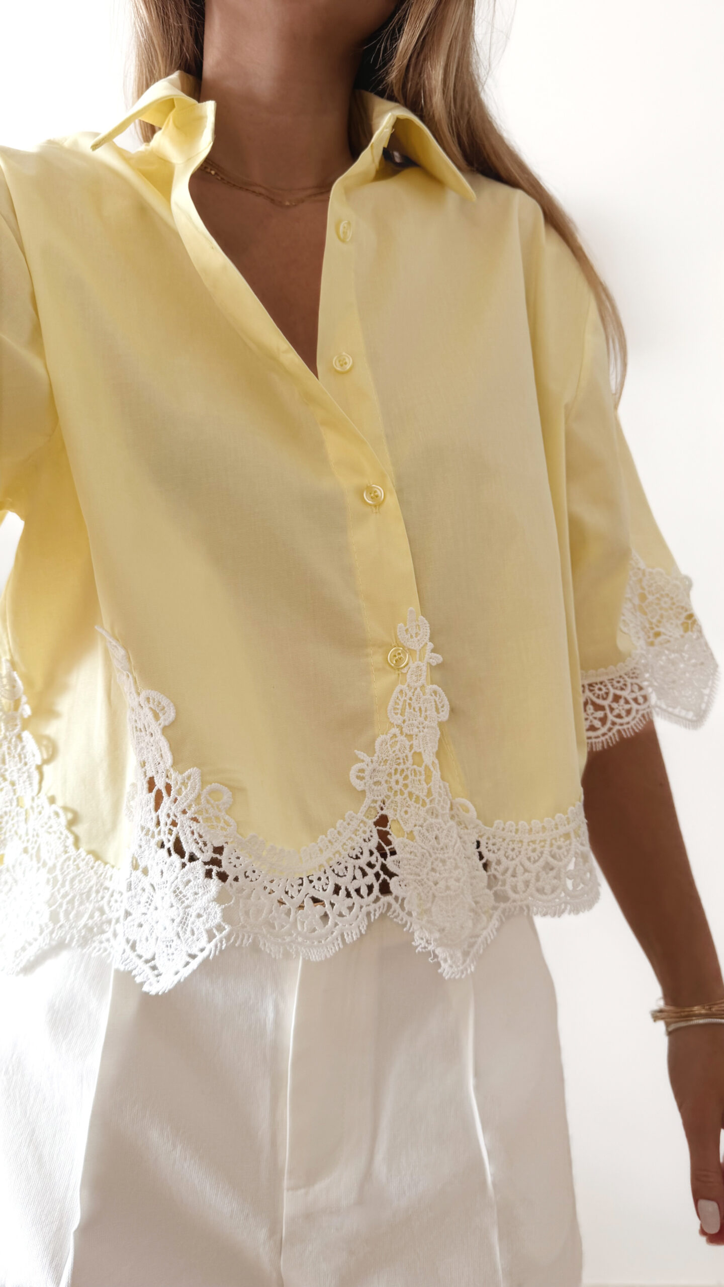 Chemise femme jaune pastel avec dentelle blanche en bas et sur les manches, manches courtes, portée avec un short blanc.