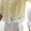 Chemise femme jaune pastel avec dentelle blanche en bas et sur les manches, manches courtes, portée avec un short blanc.