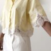 Chemise femme jaune pastel avec dentelle blanche en bas et sur les manches, manches courtes, portée avec un short blanc.