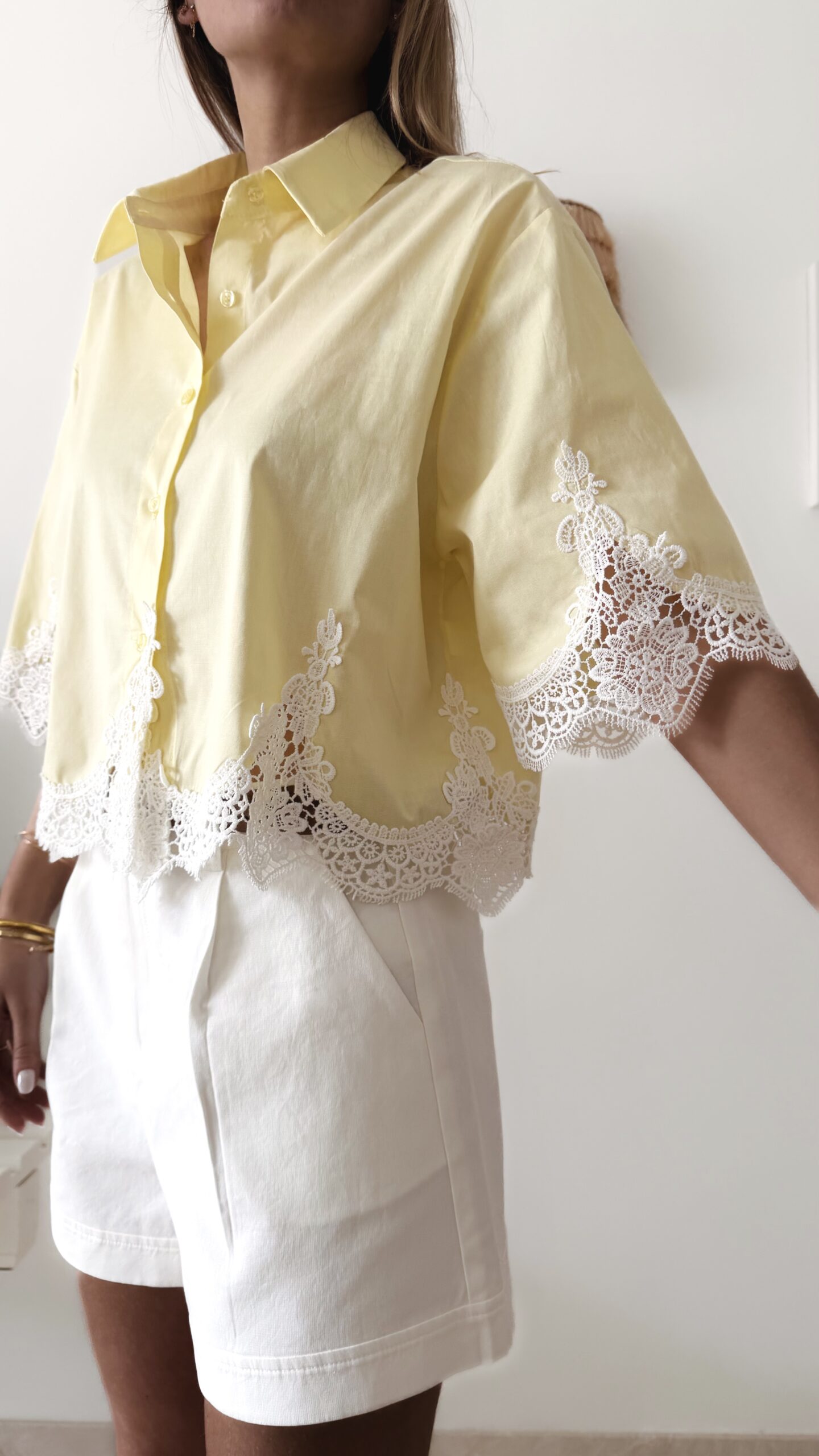Chemise femme jaune pastel avec dentelle blanche en bas et sur les manches, manches courtes, portée avec un short blanc.