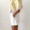 Chemise femme jaune pastel avec dentelle blanche en bas et sur les manches, manches courtes, portée avec un short blanc.