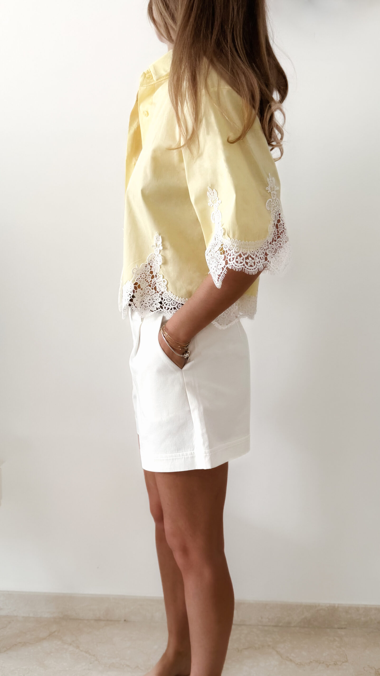 Chemise femme jaune pastel avec dentelle blanche en bas et sur les manches, manches courtes, portée avec un short blanc.