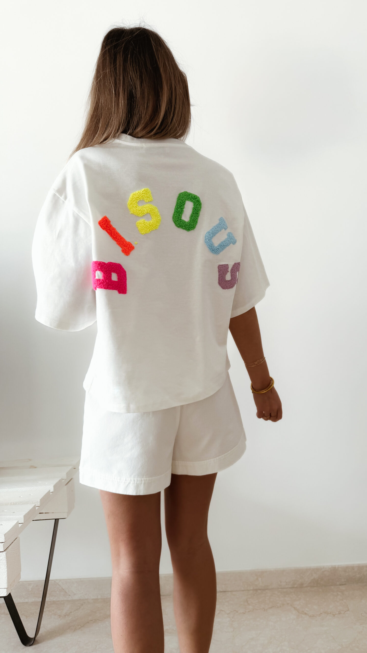 Femme vue de dos portant un ensemble blanc avec un t-shirt oversize orné de lettres colorées en relief
