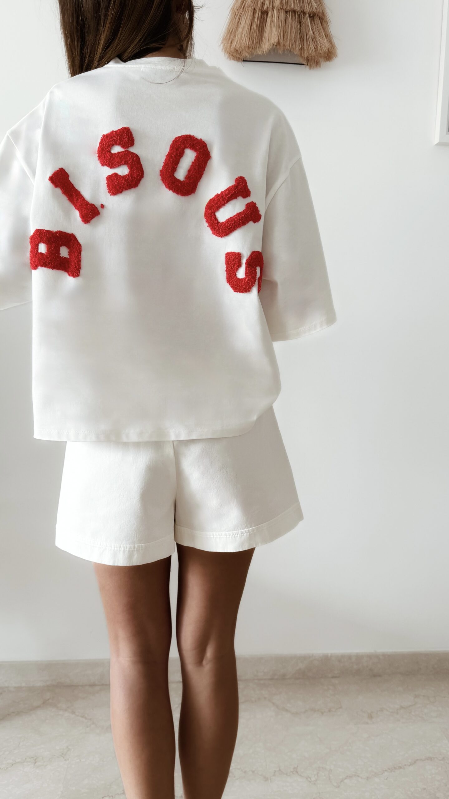 Femme vue de dos portant un ensemble blanc avec un t-shirt oversize orné de lettres rouge en relief