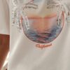 Femme portant un t-shirt blanc avec imprimé coucher de soleil et palmiers en sequins