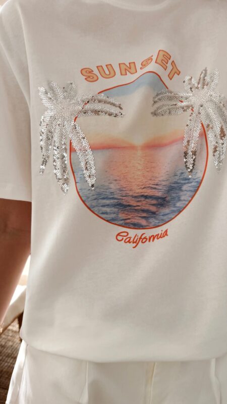 Femme portant un t-shirt blanc avec imprimé coucher de soleil et palmiers en sequins