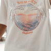 Femme portant un t-shirt blanc avec imprimé coucher de soleil et palmiers en sequins