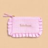 Collection de pochettes colorées à rayures et motifs vichy avec volants décoratifs et messages brodés, présentées sur un fond beige dans un style féminin et tendance.