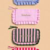 Collection de pochettes colorées à rayures et motifs vichy avec volants décoratifs et messages brodés, présentées sur un fond beige dans un style féminin et tendance.