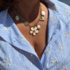 Collier chaîne dorée avec pendentif fleur blanche, perle et charms dorés porté sur peau bronzée avec tenue estivale.