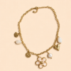 Collier chaîne dorée avec pendentif fleur blanche, perle et charms dorés porté sur peau bronzée avec tenue estivale.