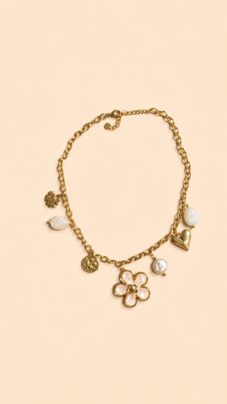Collier chaîne dorée avec pendentif fleur blanche, perle et charms dorés porté sur peau bronzée avec tenue estivale.